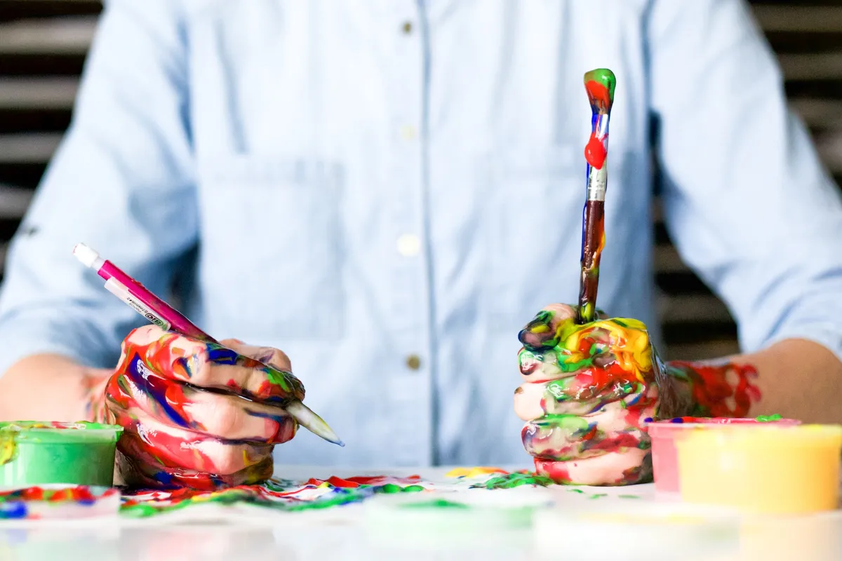 hands full of paint holding pen and brush